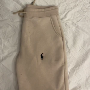 Beige mjukisbyxor Polo Ralph Lauren S - Beiga mjukisbyxor från Polo Ralph Lauren med klassisk broderad logga på benet. Byxorna har dragsko i midjan och är tillverkade i mjuk bomullsmix för extra komfort. Perfekta för chill dagar eller när du vill ha en avslappnad stil.
