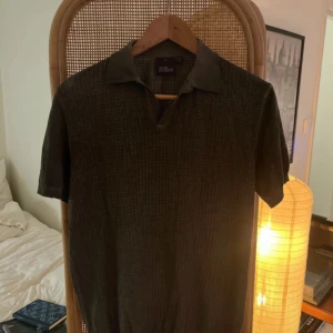 Oscar Jacobson piké - Snygg mörkgrön pikétröja från Oscar Jacobson, tillverkad i Italien. Tröjan har korta ärmar, klassisk krage och ett diskret rutigt mönster i materialet. Perfekt för dig som gillar stilrena och tidlösa plagg.