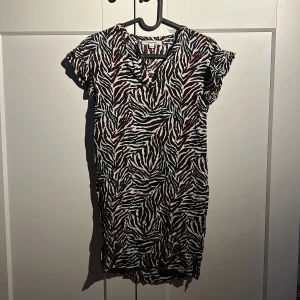 Zebramönstrad kortklänning från Garcia - Cool kortklänning från Garcia med zebramönster i mörkblå, vit och röda detaljer. Klänningen har korta ärmar och en avslappnad passform. Materialet är mjukt och bekvämt. 