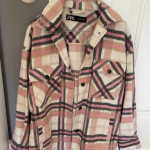 Rutig overshirt från Zara i rosa och beige - Snygg overshirt från Zara i rutigt mönster med beige, rosa och svarta toner. Jackan har klassisk krage, bröstfickor med knappar och långa ärmar. Perfekt för lager-på-lager och ger en chill vibe till din outfit.