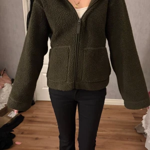 Mörkgrön teddyjacka med dragkedja - Mysig mörkgrön teddyjacka i storlek S med två stora fickor framtill och hel dragkedja. Jackan har en loose passform och är tillverkad i fluffigt fleece-material som håller dig varm. Perfekt för kyliga dagar och enkel att matcha med jeans eller leggings. Pris kan diskuteras💕