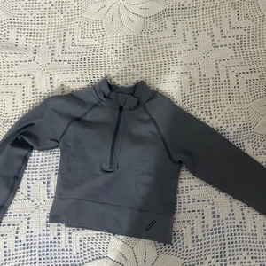 Grå croppad half zip tröja från TALA - Snygg grå croppad tröja från TALA med half zip framtill och hög krage. Tillverkad i stretchigt material med 92% polyamid och 8% elastan. Perfekt för träning eller chill, med långärmad design och stilrena sömmar.