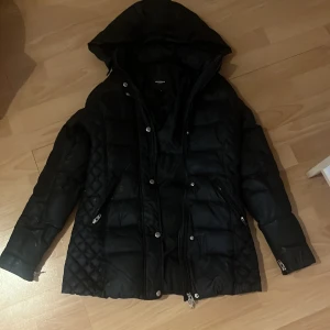 Svart pufferjacka Rockandblue med huva - Svart pufferjacka från Rockandblue med stor huva och quiltade detaljer på sidorna. Jackan har flera dragkedjor, tryckknappar och ett snyggt märke på ärmen. Perfekt för kalla dagar och har en modern, lite längre passform. Köpte två år sedan för 4000 säljer eftersom det inte är min stil längre men super fin. Pris kan diskuteras 