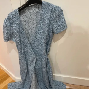 Blommig blå omlottklänning helt ny st s  - Supersöt långklänning i blått med småblommigt mönster och omlottmodell. Klänningen har korta puffärmar och markerad midja, perfekt för sommarens alla tillfällen. Lätt och luftig känsla.