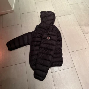 Svart Colmar dunjacka med huva - Svart dunjacka från Colmar med huva och två sidofickor med dragkedja. Köpt 2023 helt ny för 5000kr och har använt den max 2 månader varje år sen dess. Dags för ny vinterjacka för min del. Jackan har storlek 50 (M) och är som i nytt skick FÖRUTOM att jag täppt igen ett dunhål med en lapp som gjordes av en fixare på en kemtvätt. Lappen syns på bild 5 om ni ens ser den. Aldrig fått höra något om det då den inte syns i vanligt ljus och är RIKTIGT bra gjord. 