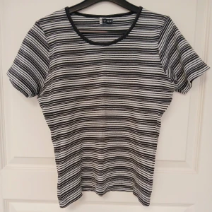 Svartvit randig topp med korta ärmar - Randig topp i svart och vitt med rund halsringning och korta ärmar. Perfekt för dig som gillar en stilren look. Tillverkad i bomull. Toppen har naturligtvis tvättats. Se bilder för skick och passform. Storlek 38/40 enligt lappen. Armhåla till armhåla är cirka 45 cm. Axelsöm till ärmslut är cirka 18-19 cm. Tvättas i 40 grader.