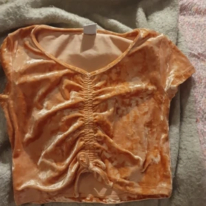 Orange sammetstopp med snörning Lindex - Superfin croppad topp i orange sammet från Lindex. Toppen har korta ärmar, v-ringning och snygg snörning framtill som ger en cool rynkad effekt. Perfekt för dig som gillar unika detaljer och mjuka material.