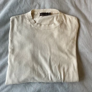 Beige stickad tröja Oscar Jacobson  - Snygg beige stickad tröja från Oscar Jacobson i storlek XL(sitter som L). Tröjan har en klassisk rund hals med ribbad kant och är tillverkad i Italien. Perfekt för dig som gillar stilrena och enkla plagg med premiumkänsla.