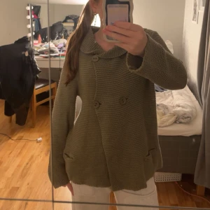 Olivgrön stickad kofta från Rabalder - Säljer en olivgrön stickad kofta från Rabalder i storlek S. Koftan har en bred krage, snygga knappar framtill och två fickor. Den är grovstickad och har långärmade ärmar med en loose passform, perfekt för att hålla sig varm under kyliga dagar.