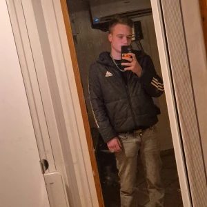 Svart pufferjacka från Adidas - Säljer en svart vintage pufferjacka från Adidas med vita ränder på ärmarna och logga på bröstet. Jackan har huva, dragkedja och en schysst, lite boxig passform. Perfekt för dig som gillar sportig stil och vill hålla dig varm under kalla dagar.