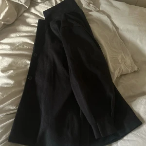 Svart kappa med bälte och knappar - Säljer en svart kappa med snyggt bälte i midjan och klassiska knappar framtill. Jackan har långärmade ärmar och en stilren, rak passform. Perfekt för dig som gillar minimalistisk och clean look. Materialet känns mjukt och är troligtvis ull eller polyester. Passar även M, kan skicka bättre bilder. 