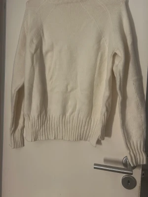Vit stickad tröja med ribbade muddar - Mysig vit stickad tröja med lång ärm och breda ribbade muddar vid ärmslut och nederkant. Tröjan har en enkel, clean look och är perfekt för lager på lager under kyliga dagar. Passar dig som gillar en klassisk och stilren vibe. Aldrig använd