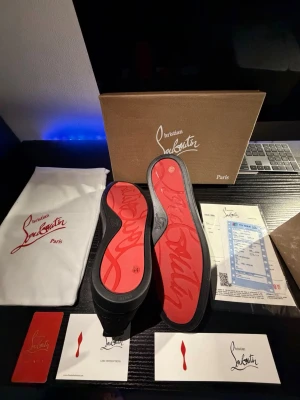 Christian Louboutin svarta sneakers mocka - Svarta sneakers från Christian Louboutin i lyxig mocka med signaturröd sula och broderad logga på hälen. Skorna har rund tå, platt sula och snörning framtill. Kommer med originalkartong, dustbag och certifikat. Helt oanvända, pris kan diskuteras!
