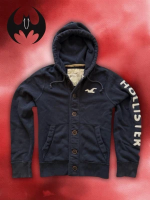 Vintage kofta Hollister (Sällsynt) - Sällysnt mörkblå kofta med tryck och broderat vitt Hollister-tryck på bröstet och höger armen | extremt svårt att hitta och limiterad | fint skick | size M / L | längd: 68 cm Axelbredd: 46cm Armlängd: 72cm Midja (runt): 110 cm