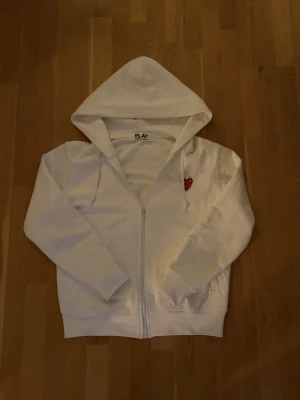 Vit Comme des Garçons hoodie - Sjukt snygg vit CDG zip hoodie med den ikoniska loggan på bröstet. Storlek M, skick 9/10 någon fläck som ser ut som från en penna, syns knappt vid användning. Borde gå bort i tvätten. BVSA, Skriv för frågor!🙌☺️