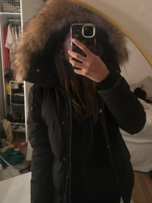 Svart dunjacka Hollies med pälskant - Säljer en svart dunjacka från Hollies i storlek 34. Jackan har stor fluffig huva med beige pälskant, dragkedja och knappar framtill samt flera fickor. Insidan har coolt tryck och orange piping. Perfekt för kalla dagar och riktigt snygg vinterstil.