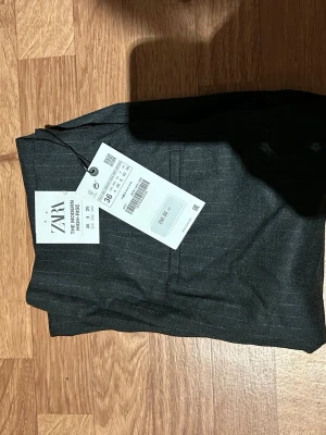 Mörkgrå högmidjade kostymbyxor Zara - Säljer ett par mörkgrå kostymbyxor från Zara i modellen The Modern High-Rise. Byxorna har diskreta tunna ränder, hög midja och klassisk rak passform. Perfekta för en clean och stilren look. Storlek 36.
