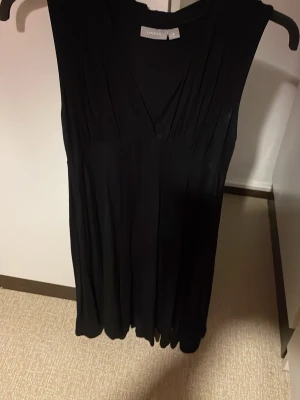 Svart omlottklänning från Lindex - Svart ärmlös omlottklänning från Lindex i mjukt och följsamt material. Klänningen har v-ringning framtill och knytband i ryggen för extra detalj. Perfekt för dig som gillar enkel men snygg stil. Viscos o elastan. Säljs på fler sidor.