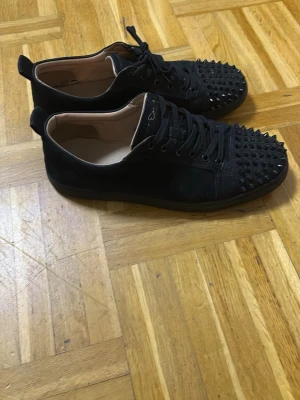 Svarta Loubs med röd sula - Säljer ett par svarta sneakers i mocka med svarta nitar över tån och klassisk röd sula. Boxen finns också med skor påsen. 