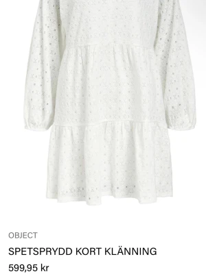 Vit spetsprydd student klänninh - Supersöt vit kort klänning från Object med spetsdetaljer och v-ringning. Klänningen har långa ärmar med resår vid ärmslut och volang nedtill. Helt ny!!