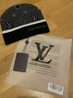 Lv svart sett - Säljer en snygg svart och gråt sett från Lv  med klassiskt LV-monogram och blommönster. Settet  har en vit rand och Lv -logga broderad framtill. Stickad i mjukt material och levereras med tag och originalpåse.