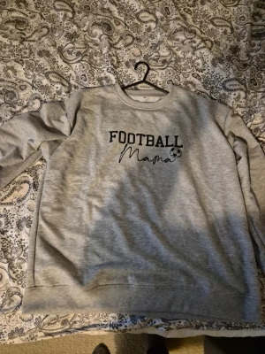 Grå sweatshirt 'Football Mama' XXL - Säljer en grå sweatshirt i storlek XXL med texten 'Football Mama' och en liten fotboll på bröstet. Tröjan har rund halsringning och långa ärmar. Perfekt för dig som älskar fotboll och vill ha en chill och bekväm stil.