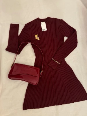 Vinröd ribbstickad klänning – figurnära & stilren (nyskick) från H&M - Produktbeskrivning: •En vinröd ribbstickad klänning. •I figurnära modell. •Helt oanvänd med lapp kvar. •Ribbstickat material som ger en smickrande silhuett. •Stretchigt och bekvämt tyg. •Perfekt längd att bära med boots, klackar eller sneakers. •Ett tidlöst och feminint plagg som passar lika bra till vardag som till finare tillfällen. •Smyckena och väskan följs inte med - de visas endast i den första bilden som tips om hur klänningen kan stylas. •Passar bra till kallare vinter och vår dagar. 