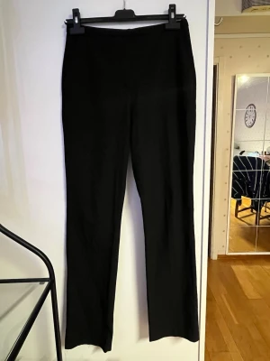 Svarta raka kostymbyxor - Säljer ett par svarta kostymbyxor med rak passform och hög midja. Byxorna har en clean look utan synliga detaljer framtill. Materialet känns mjukt, vilket gör dem riktigt sköna att bära.