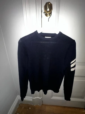 Mörkblå stickad tröja Zadig & Voltaire - Snygg mörkblå stickad tröja från Zadig & Voltaire med vita ränder på ena ärmen. Rund hals och långärmad modell, perfekt för dig som gillar stilrena detaljer med en twist. Passar dig som vill ha en cool och enkel look.