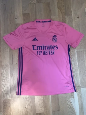 Rosa Real Madrid Tröja  - Bilderna visar en rosa Real Madrid fotbollströja från Adidas med mörkblå detaljer och logga, om ni har frågor eller funderingar så är det bara att skriva. Tack Mvh 😊