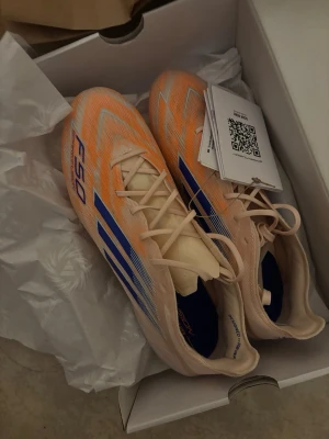 Adidas F50 Spark Fusion fotbollsskor - Säljer ett par Adidas F50 Spark Fusion fotbollsskor i ljusbeige med orange och blå detaljer. Skorna har snörning, spetsig tå och en glansig, iriserande sula med dobbar. Medföljer extra innersulor och en matchande skopåse. Perfekt för dig som vill sticka ut på planen. pris kan diskuteras!