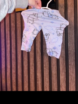 Ljusblå byxor med nalle puh storlek 62 - Supersöta ljusblå byxor med gulligt mönster av nalle puh, moln och stjärnor. Byxorna har resår i midjan och är gjorda i mjukt bomullstyg, perfekta för chill dagar hemma. Passar perfekt till små barn som gillar lekfulla prints. Storlek 62