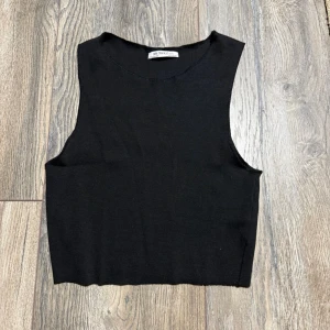 Svart ribbad linnetopp från Zara - En enkel och stilren svart linnetopp från Zara med ribbad struktur. Toppen är ärmlös och har en croppad passform som passar perfekt till höga jeans eller kjol. Materialet är mjukt och stretchigt för en bekväm känsla.