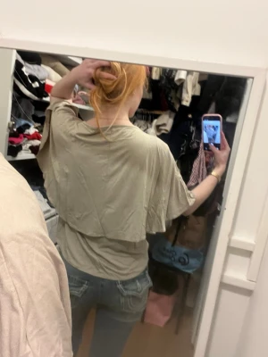 Beige T-shirt med poncho på baksidan  - En flowig T-shirt som ser ut som en poncho på ryggen.