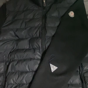 Moncler cardigan - Snygg svart pufferjacka från Moncler med klassisk logga på ärmen och dragkedja framtill. Jackan har quiltad framsida och släta ärmar, perfekt för kyliga dagar. Stilsäker och enkel att matcha med olika outfits.