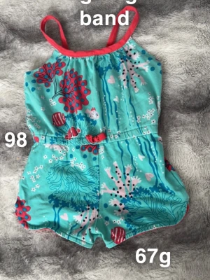 Turkos byxdress med havsmönster - Säljer en söt turkos byxdress med smala axelband och färgglatt havsinspirerat mönster med koraller, fiskar och hjärtan. Dressen har en liten rosett i midjan. Perfekt för varma dagar!🌸 Fint använt skick. Förlängsbara band. Storlek 98