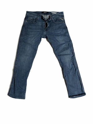Blå Replay jeans straight fit - Snygga blå jeans från Replay med klassisk femficksdesign och raka ben. Jeansen har en mörk tvätt och tydliga sömmar, perfekt för en avslappnad stil. Materialet är slitstarkt jeans och passformen är normal med midja.