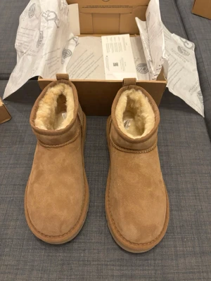 UGG boots  - UGG boots i klassisk beige färg med mjukt fårskinnsfoder och ovandel i mocka. Skorna har rund tå, platt sula och dragflik bak för enkel påtagning. Perfekta för kalla dagar och ger en cozy vibe till din outfit.