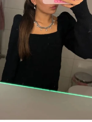 Svart stickad topp med puffärm - Säljer en svart stickad topp med fyrkantig ringning och puffärmar. Toppen har lång ärm och en tight passform som ger en snygg siluett. Perfekt att styla med smycken för en trendig look.