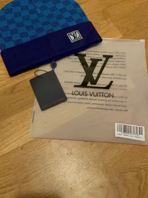 Blå  LV set - Säljer en snygg settet från Louis Vuitton i blått och lila med rutigt mönster och LV-logga framtill. Settet är stickad och har en bred, enfärgad kant. Perfekt accessoar för att lyfta din stil.