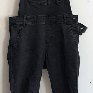 Black jean overal. Long skinny pants. Closing with bottons on the left side. Pocket on the chest and 4 on the pants.