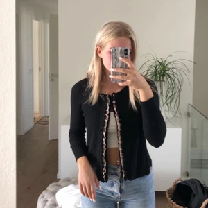 Kofta - Svart kofta med beiga volanger precis vid knäppningen. Kommer tyvärr inte till användning. Frakt tillkommer!