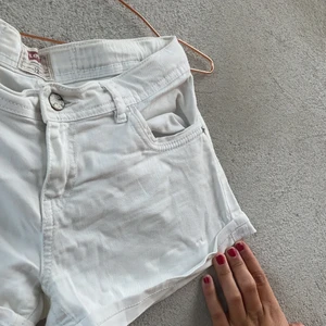 Vita Levis shorts  - Fina vita basis Levis shorts med silvriga nitar vid framfickan, retro knapp med text på. På baksidan sitter ett litet märke på högra sidan av bakre högrefickan samt ett större märke ovanför. Skönt, stretchigt jeans material. Lätta att skvätta 