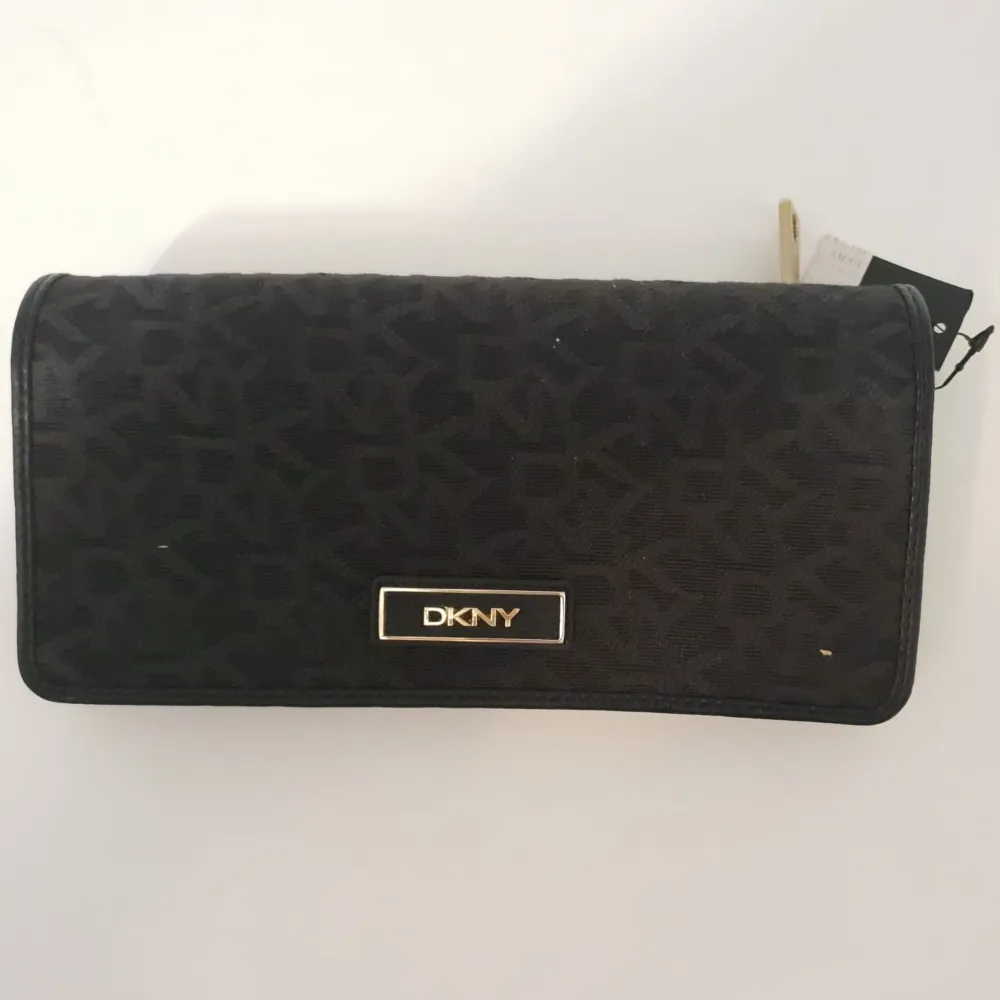 Oanvänd DKNY plånbok med alla lappar kvar. Svartmönstrad med gulddetaljer. Inköpt i New York och sedan har den legat i en låda.   Mått ca:19 cm lång, 10 cm hög och 3 cm djup.. Accessoarer.