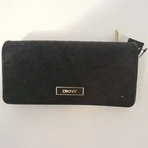 Oanvänd DKNY plånbok med alla lappar kvar. Svartmönstrad med gulddetaljer. Inköpt i New York och sedan har den legat i en låda.   Mått ca:19 cm lång, 10 cm hög och 3 cm djup.