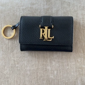Ralph Lauren liten plånbok  - Äkta Ralph Lauren. Svart skinn med gulddetaljer.  Nyckelring finns fäst i plånboken. Myntfack. Plastficka baktill. Toppskick. Storlek 11cm*7cm. Nypris ca 800kr