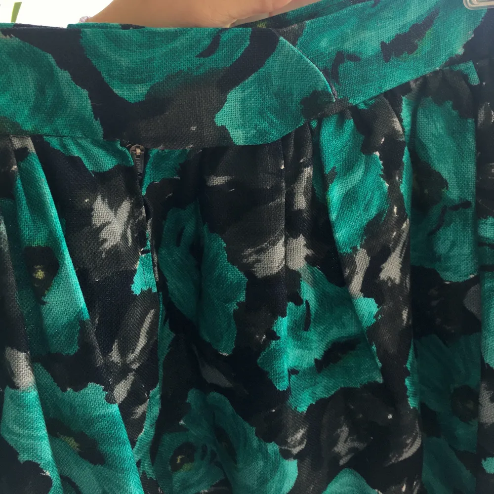 En oanvänd blommig grön kjol storlek S, kanske M. Den gjordes på 1960-talet i Italien. Kjolen är av ett tjockt lin tyg. Det finns en dragkedja och två knäppningar där bak. Frakt ingår ej . Kjolar.