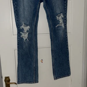 Jeans med slitningar - Snygga jeans från HM med hög midja, bootcut och hål på bägge knäna. Bara använts en gång då jag inte tyckte att de passade mig. Storlek 40 men något små i storleken.  