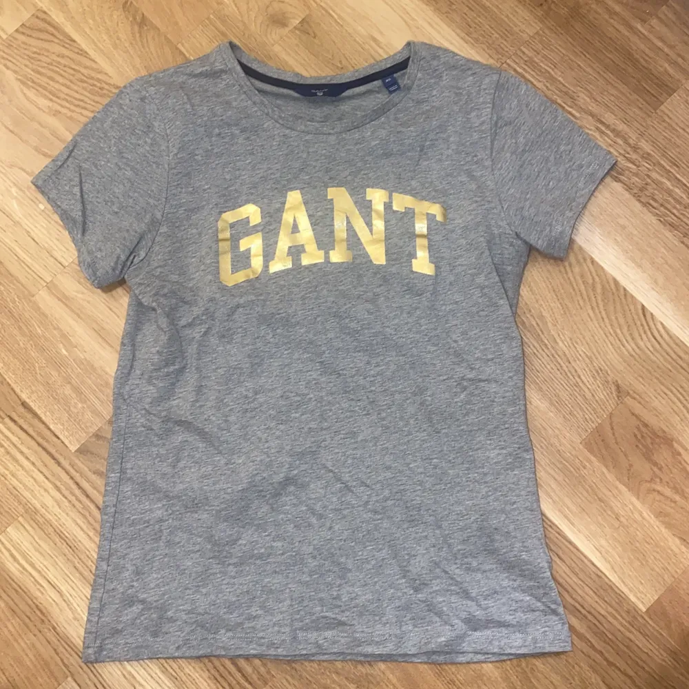 Grå T-shirt från GANT med guldigt tryck. Storlek XS. Knappt använd!. T-shirts.