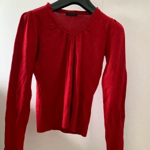 Topp - En röd topp med v-ringning med fina knappdetaljer på nedre delen av ärmarna